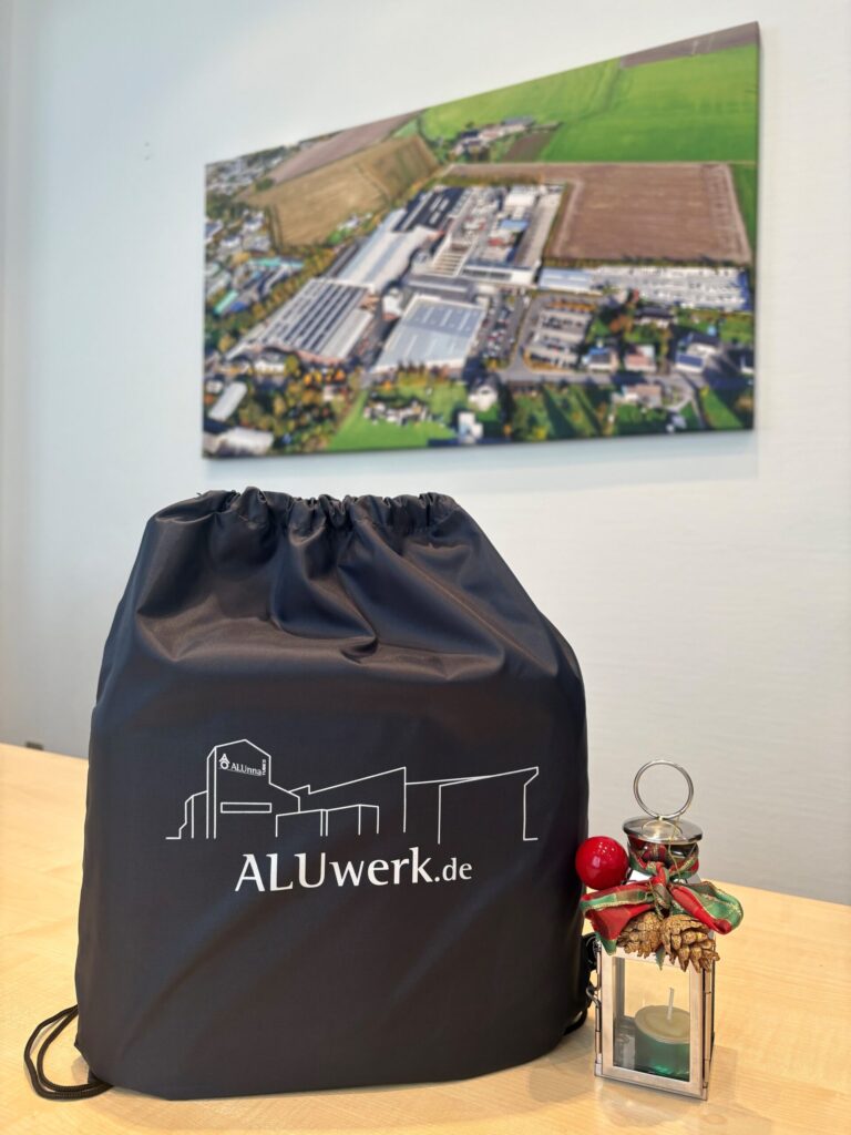 ALUwerk – mit ALUwerk-Logo bedruckter Stoffbeitel auf einem Tisch neben kleiner Weihnachtsdekolampe